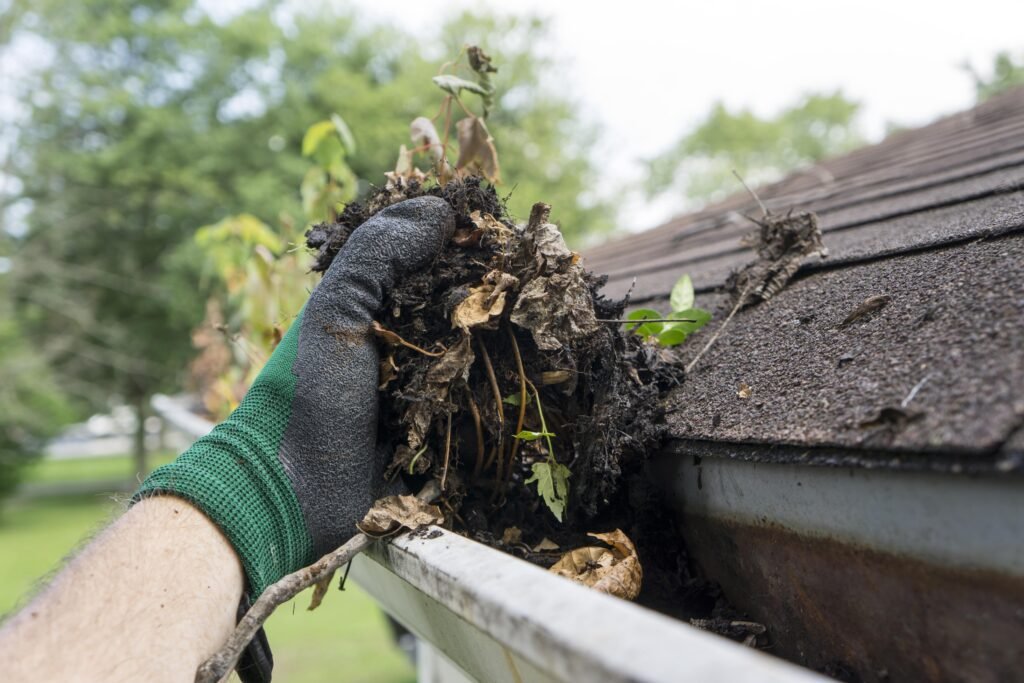 Gutter cleaning near me in Marysville, WA, with a hand removing debris from a dirty gutter.