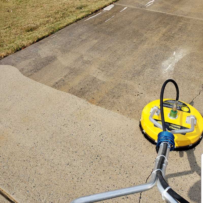 Residential driveway pressure washing in Arlington WA using a surface cleaner, showing dirty to clean results.